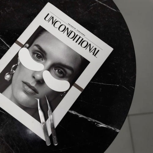 photo noire et blanche avec une table en marbre noir, une affiche avec un visage et des patchs et des pinces d'extensions de cils sur le visage